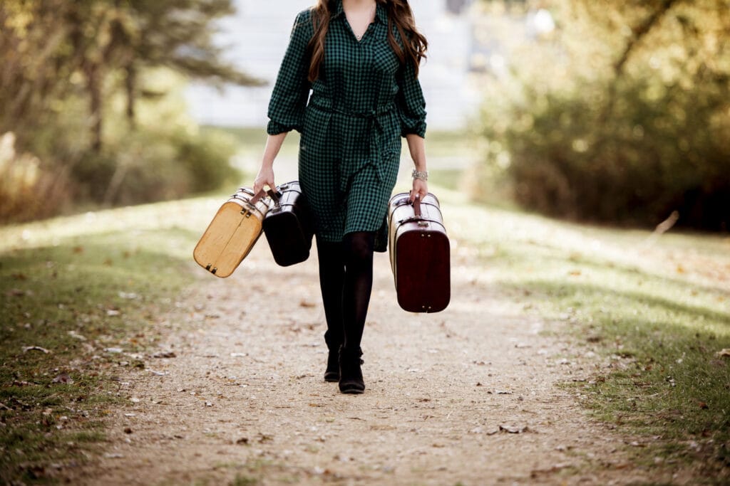 Moteris einanti laikydama seną lagaminą neryškiame fone nepanaudotos atostogos išeinant iš darbo