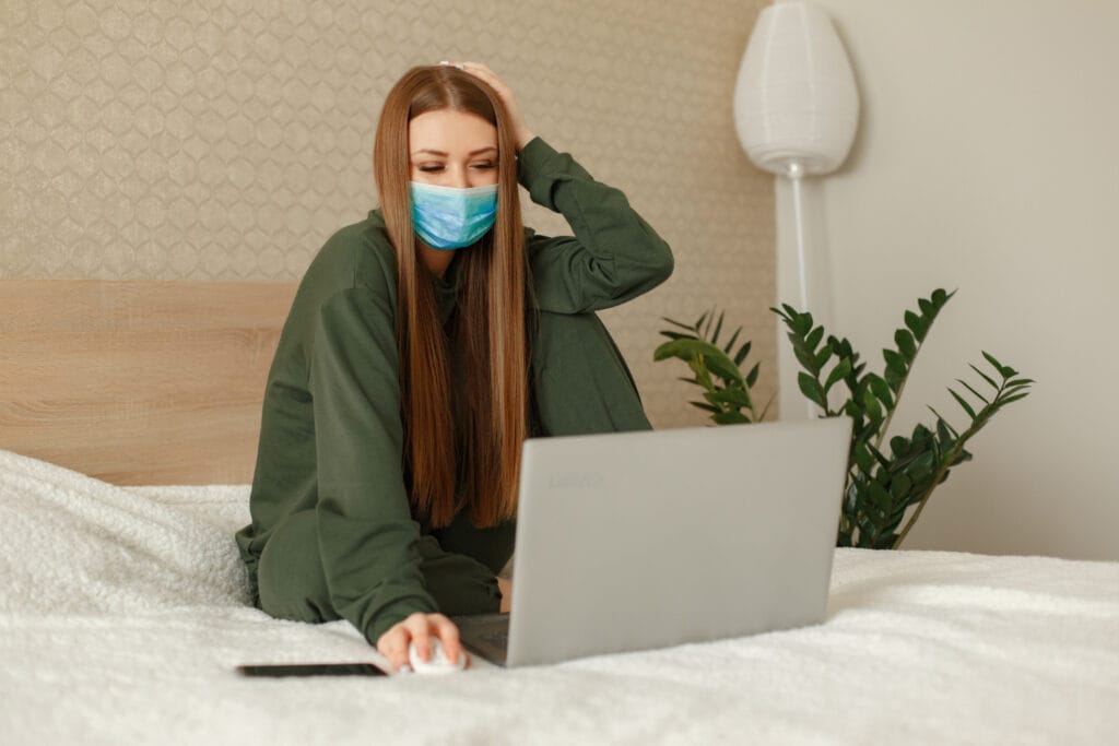 Moteris sėdi ant lovos ir naudojasi nešiojamuoju kompiuteriu kaip mokamas biuletenis