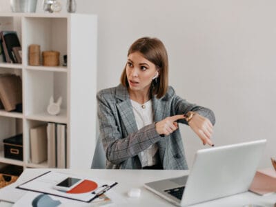 Stilingai apsirengusi viršininkė rodo į laikrodį kalbėdama apie pavaldinio vėlavimą išėjimas iš darbo bandomuoju laikotarpiu