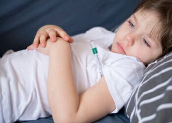 Vaizdas iš priekio į lovoje sėdintį sergantį vaiką