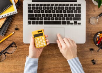 Vaizdas iš viršaus į mokinį laikantį skaičiuotuvą kaip apskaiciuoti pvm