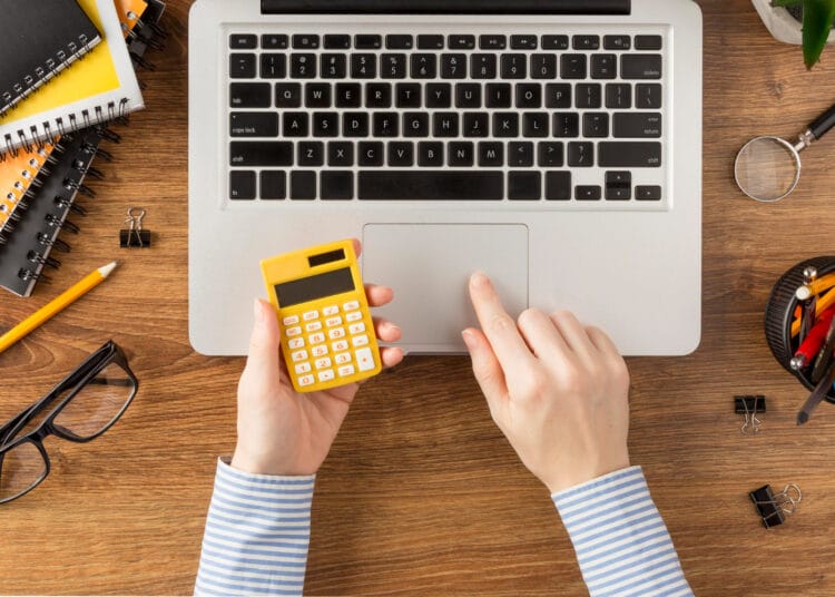 Vaizdas iš viršaus į mokinį laikantį skaičiuotuvą kaip apskaiciuoti pvm