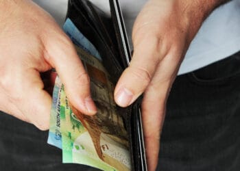 Dideliu kampu nufotografuotas žmogus dedantis pinigus į odinę piniginę kada vmi grazinas permokas