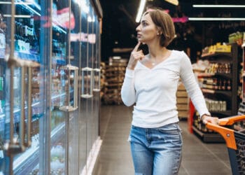 Moteris apsiperkanti maisto prekių parduotuvėje, prie šaldytuvo