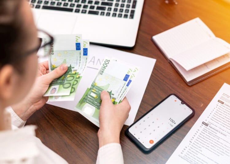 Moteris dirbanti su finansais ir skaičiuojanti pinigus ant stalo Smertphone užrašų knygutė kas yra npd