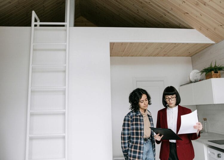 Moteris raudonu paltu rodanti dokumentus šalia stovinčiai moteriai