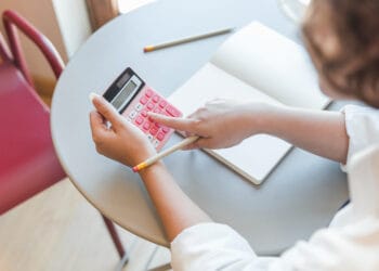 Pasėlių paauglys prie stalo naudojasi skaičiuotuvu kaip apskaiciuoti pvm