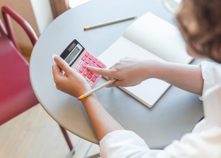 Pasėlių paauglys prie stalo naudojasi skaičiuotuvu kaip apskaiciuoti pvm