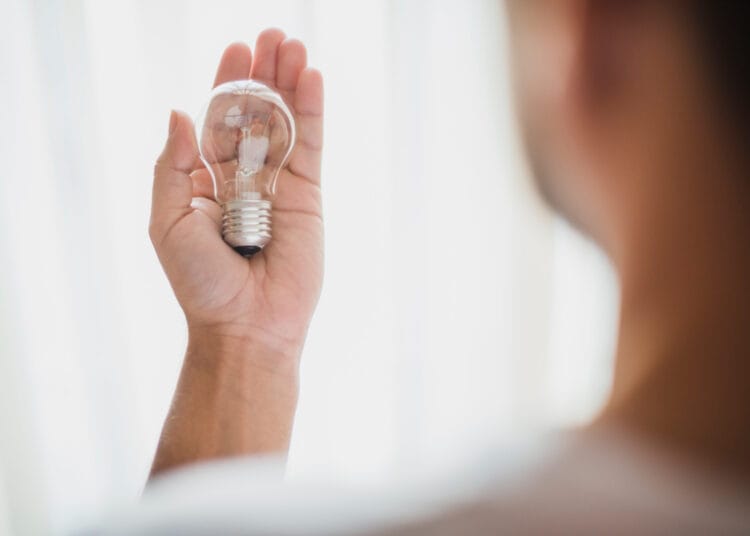 Vyro rankos vaizdas iš nugaros rodantis permatomą elektros lemputę