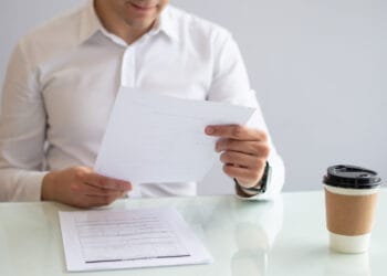 Artimas kadras kuriame šypsosi jaunas verslininkas žiūrintis į dokumentą individuali veikla ar verslo liudijimas