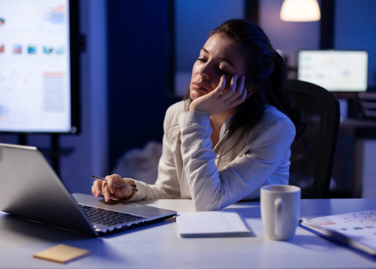 Išsekęs laisvai samdomas darbuotojas užmiega prie nešiojamojo kompiuterio vėlyvą naktį tikrindamas finansines ataskaitas įmonės biure virsvalandziai